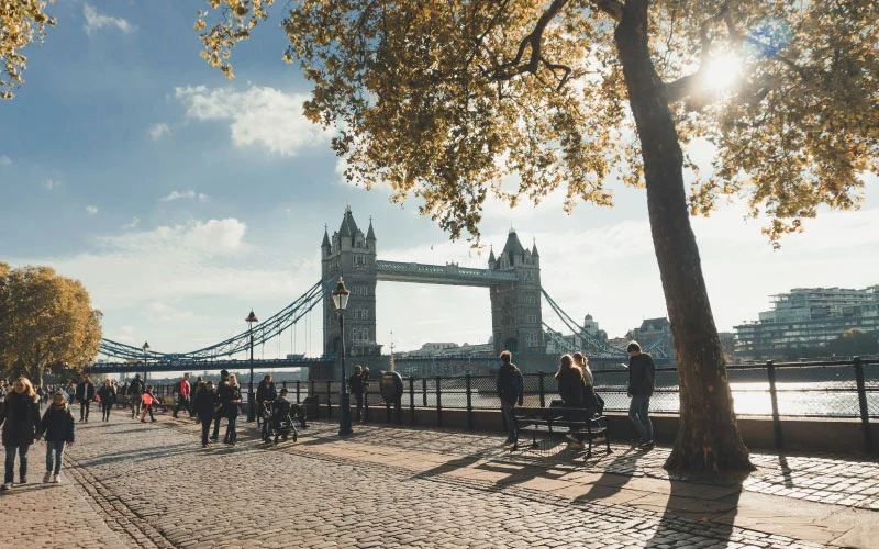 People boarding a modern coach by the River Thames, with Tower Bridge in the background.