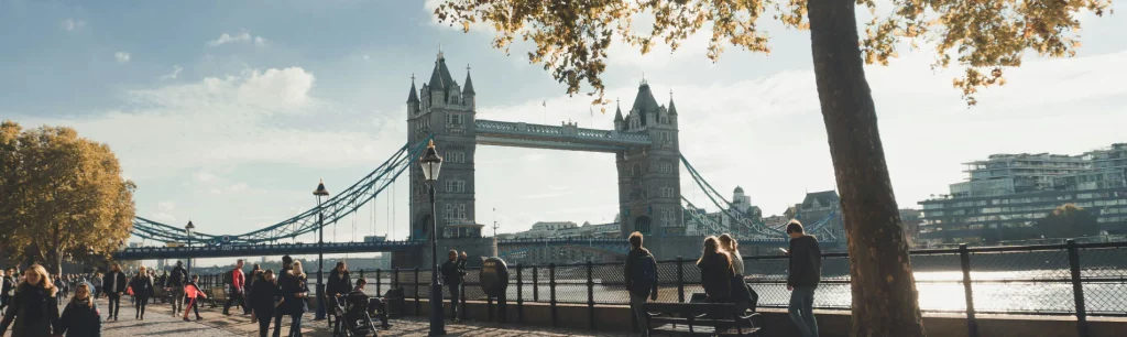 People boarding a modern coach by the River Thames, with Tower Bridge in the background.